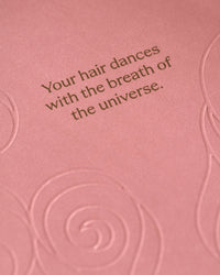 Imagen de acercamiento a la frase decorativa del empaque "Your hair dances with the breath of the universe".